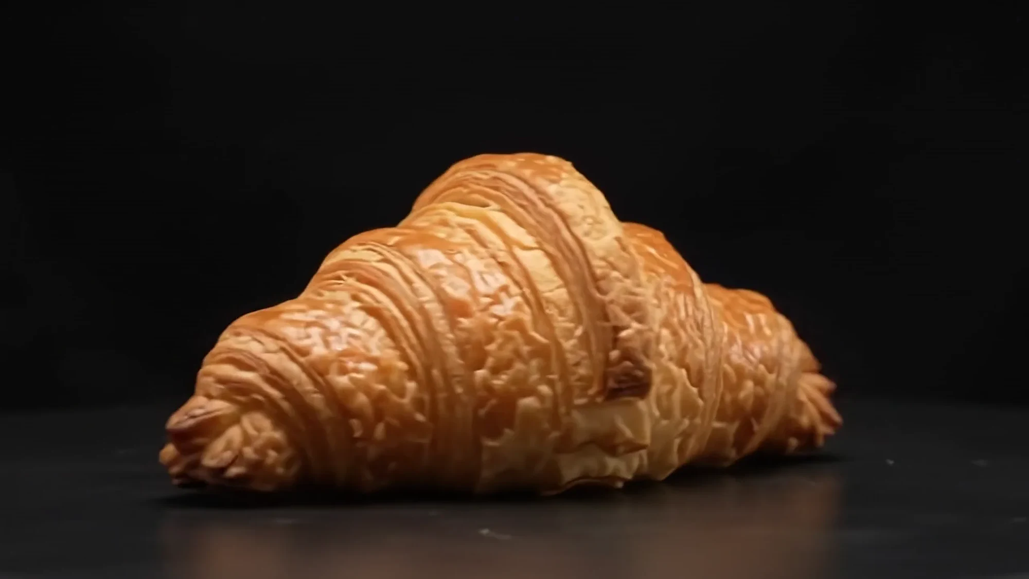 Golden croissant with crisp folded ridges against a dark background