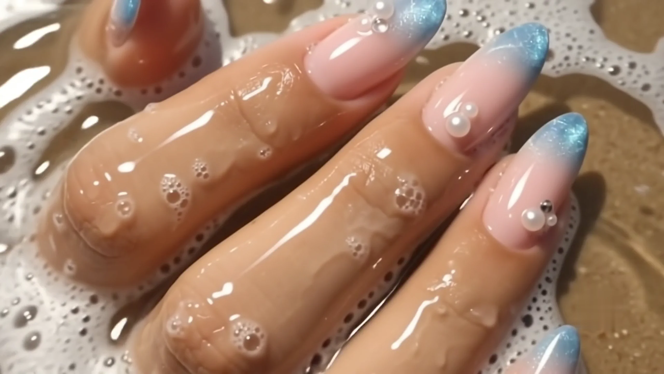 Pearl-detailed ocean-blue French manicure emerging from a wave