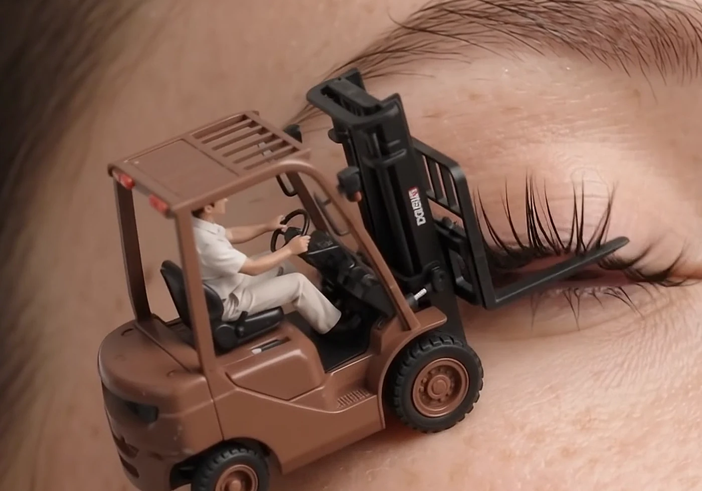 The toy forklift loading a strip of lashes beside a freckled eye