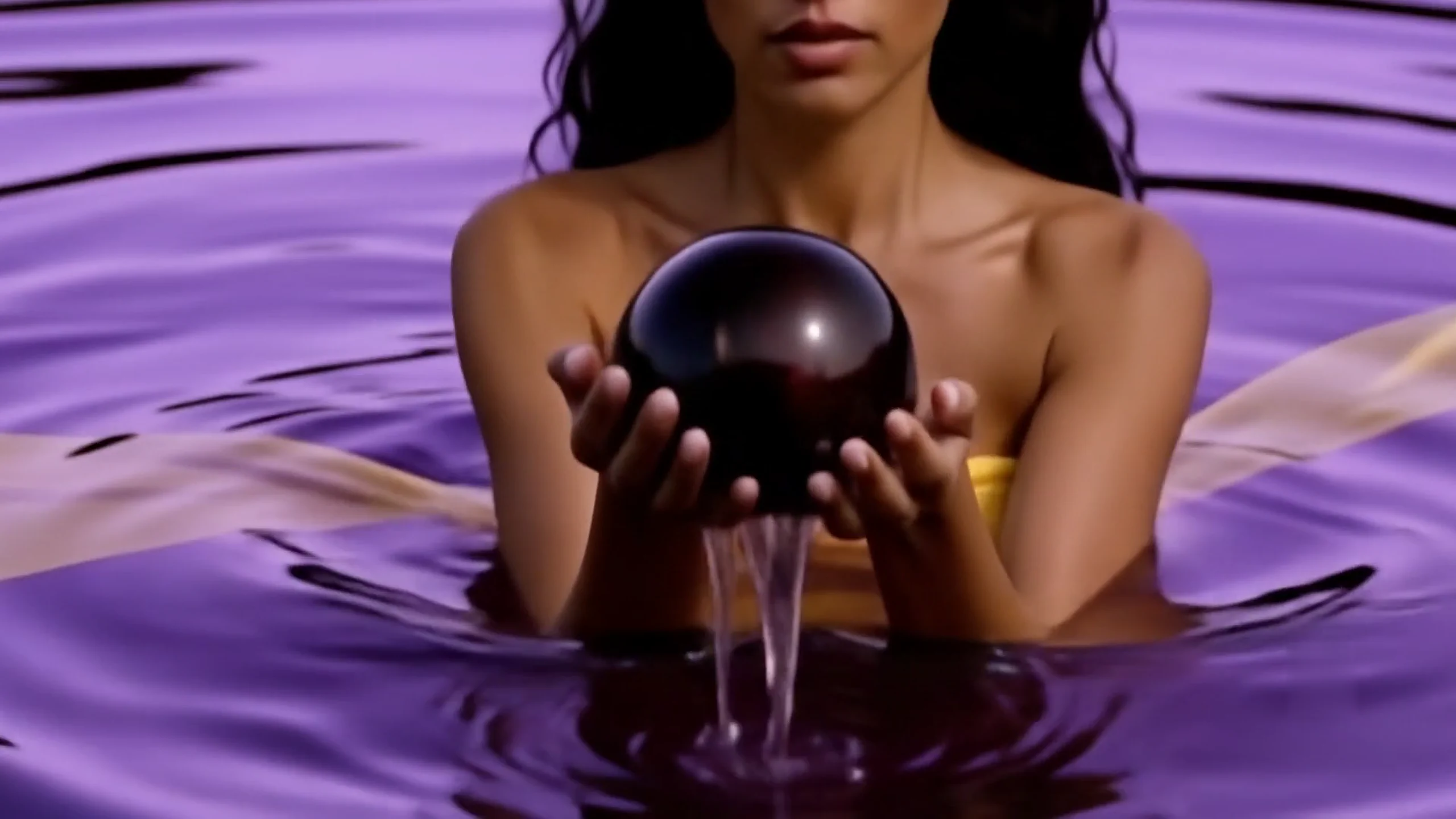 Editorial close-up of a model holding a dark pearl above violet water